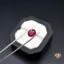 Tweezers holding a round pink gemstone over a black jewelry box