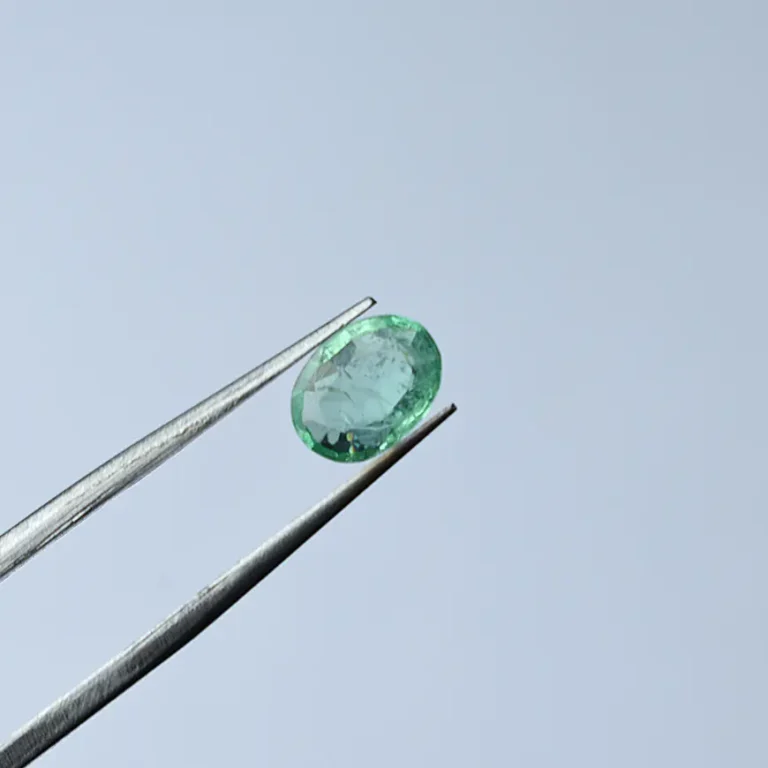 Oval cut natural emerald held with tweezers