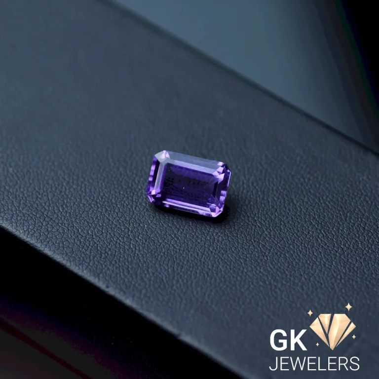 Emerald-cut purple gemstone on a dark gray leather surface
