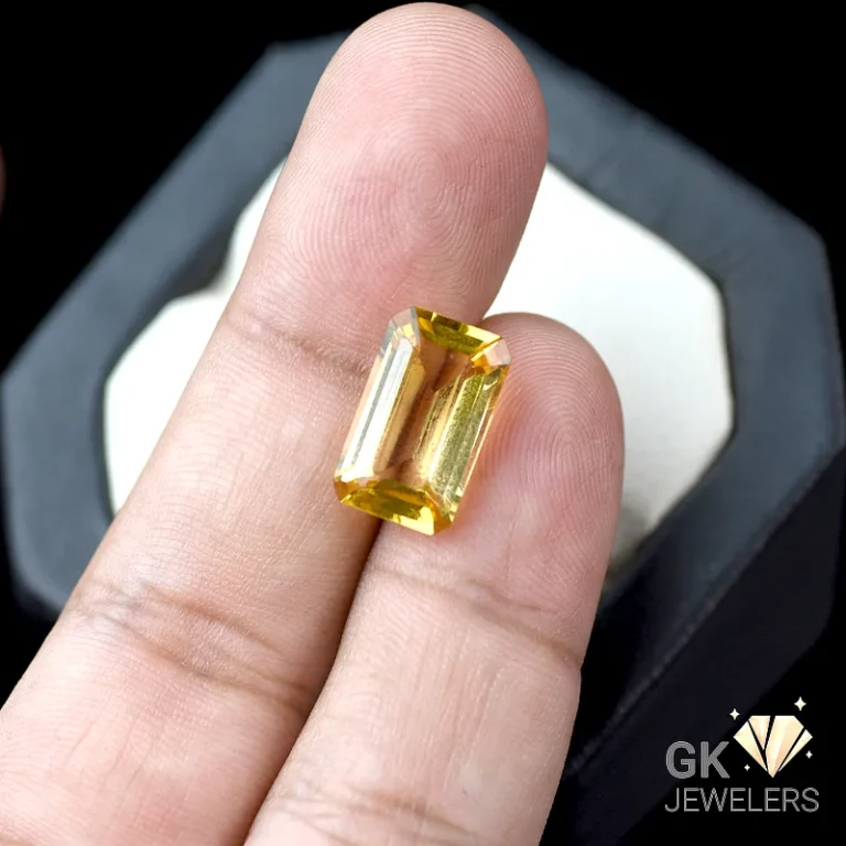 Yellow citrine gemstone held between fingers over a jewelry box