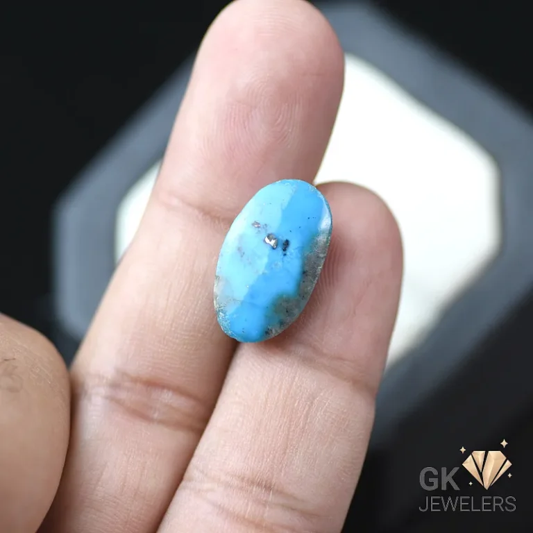 Turquoise oval cabochon gemstone on a person's fingertips