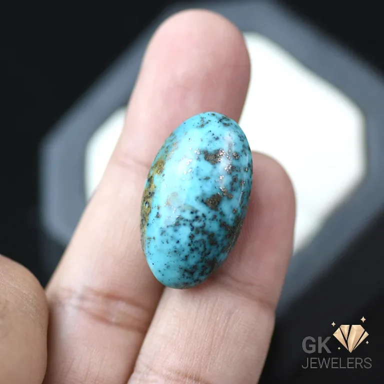 Turquoise gemstone with black speckles held between fingers