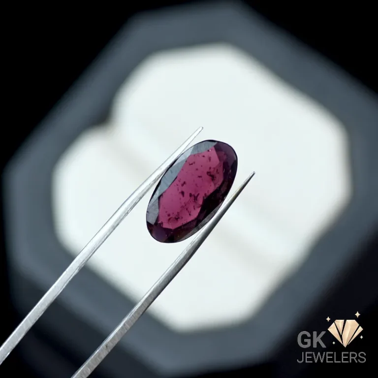 Oval ruby gemstone held by tweezers against a dark background