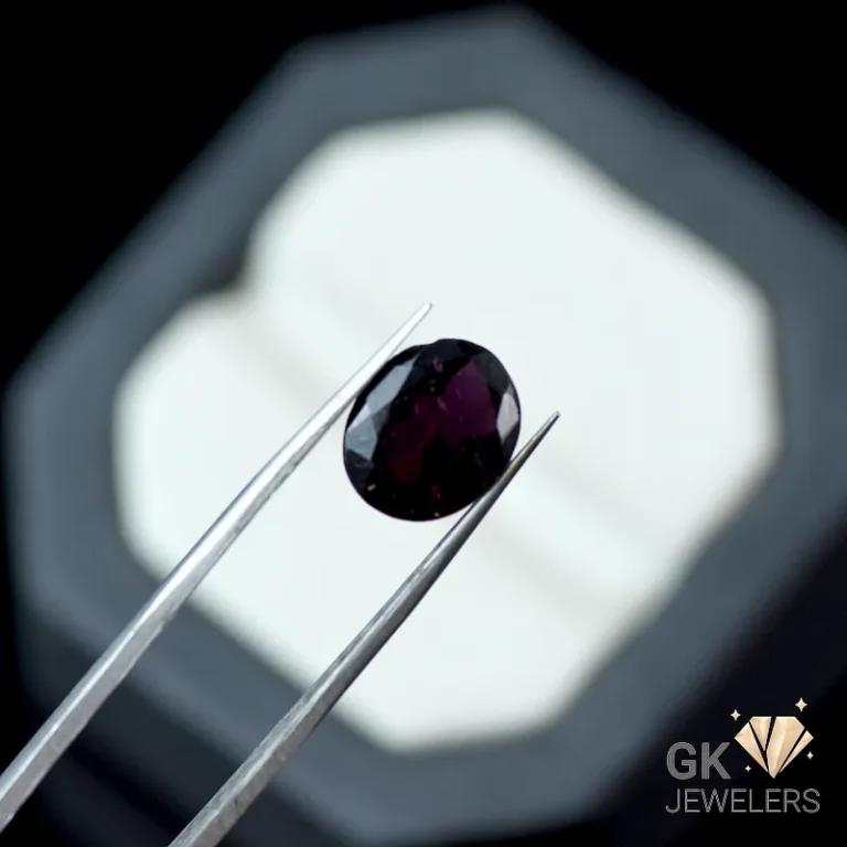 Oval-cut garnet gemstone held by tweezers against a blurred jewelry box background