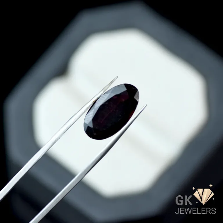 Dark red oval-cut gemstone held by silver tweezers