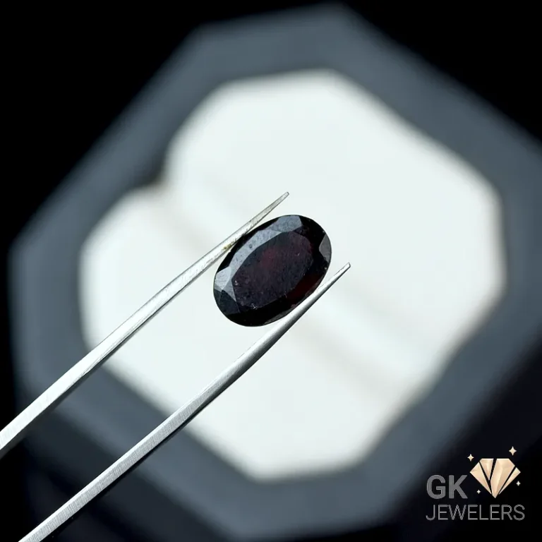 Oval dark red garnet gemstone held by silver tweezers