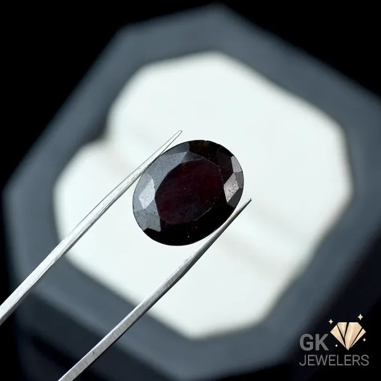 Faceted dark garnet gemstone held by silver tweezers