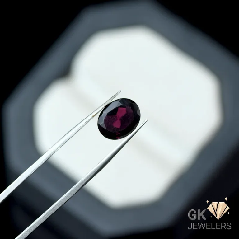 Oval-cut dark red garnet gemstone grasped by silver tweezers