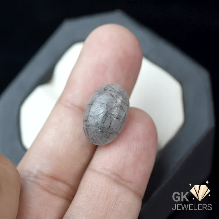 Gray Tourmaline gemstone with rutile inclusions held between fingers