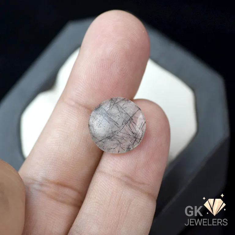Round black rutilated quartz gemstone on fingertips
