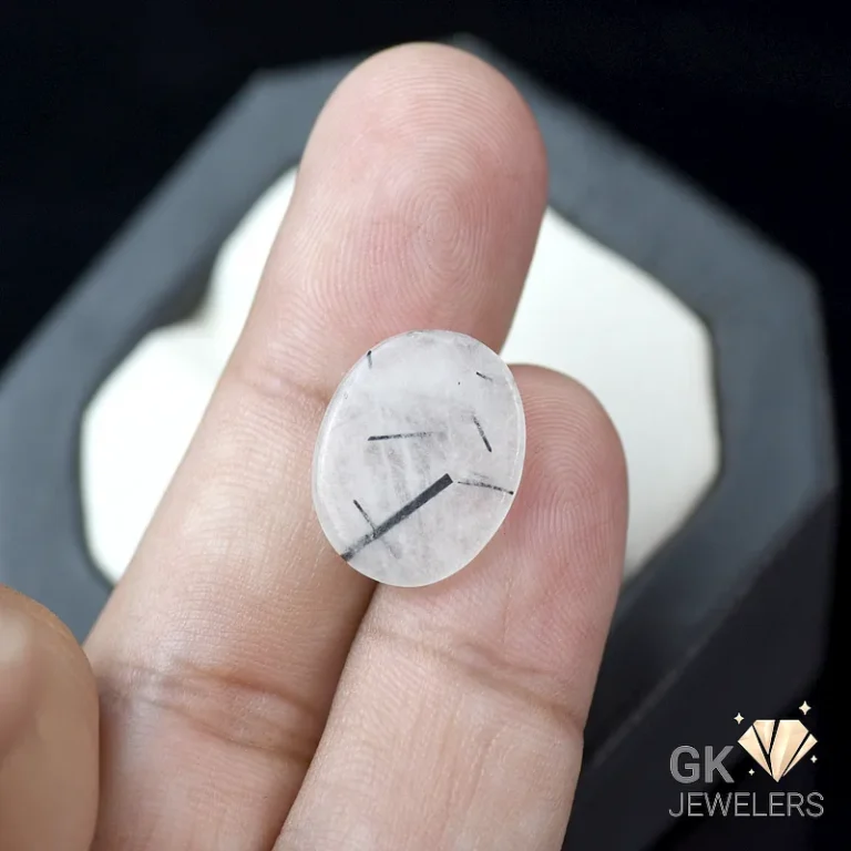 White round gemstone with black inclusions held between fingers