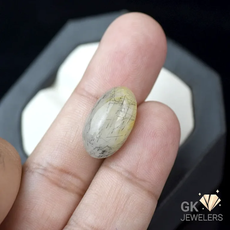Oval cabochon rutilated quartz gemstone with golden rutile inclusions held between fingers