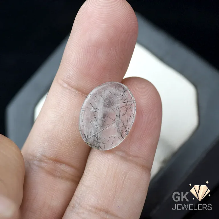 Oval rutilated quartz gemstone held between fingers