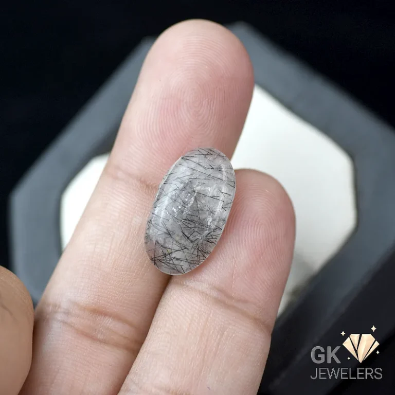 Oval rutilated quartz gemstone held between fingers