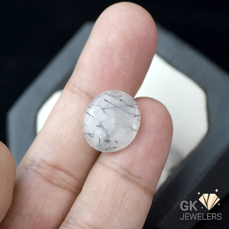 White tourmalinated quartz gemstone held between fingers