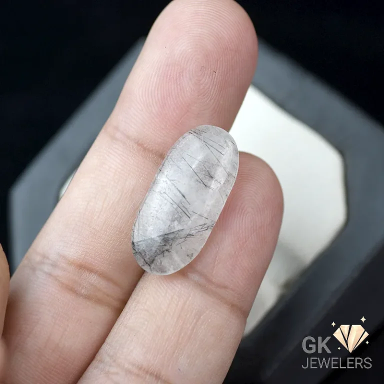 Oval white gemstone with black inclusions on fingertips