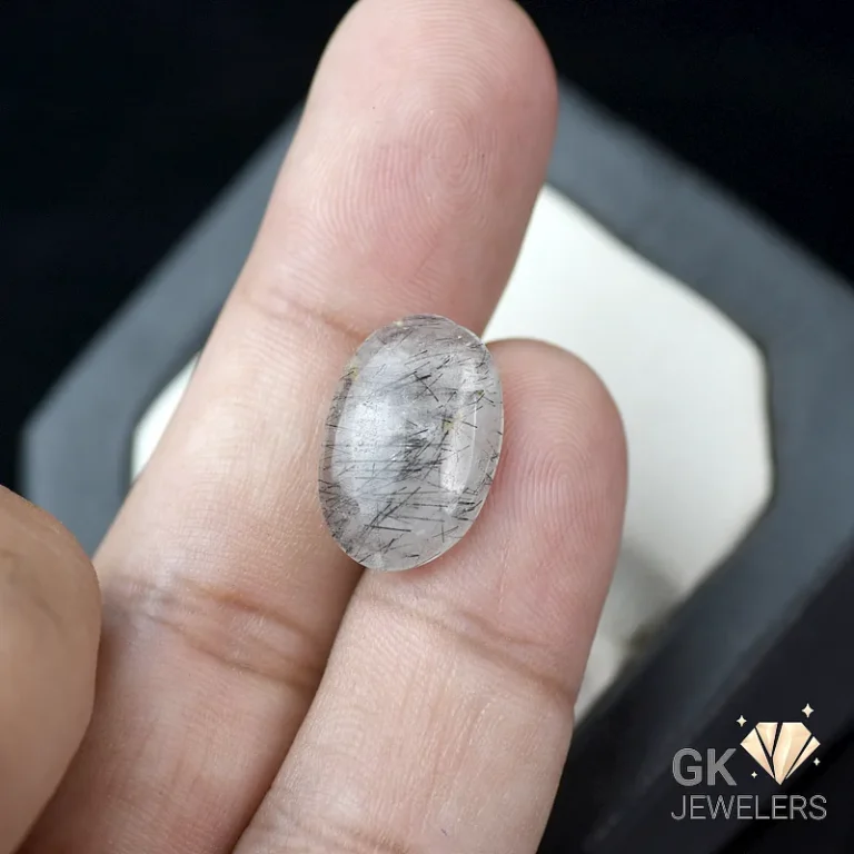 Oval cabochon gemstone with dark inclusions between fingers