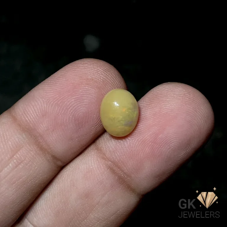Oval yellow opal gemstone resting on fingertips against a dark background