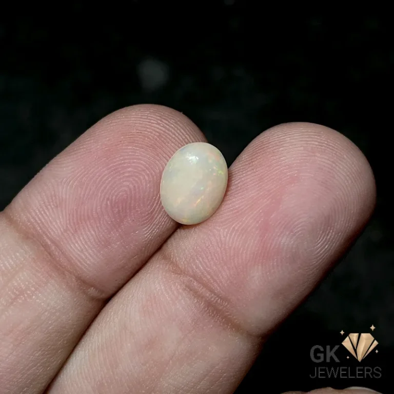 Oval opal gemstone resting on fingertips against a dark background
