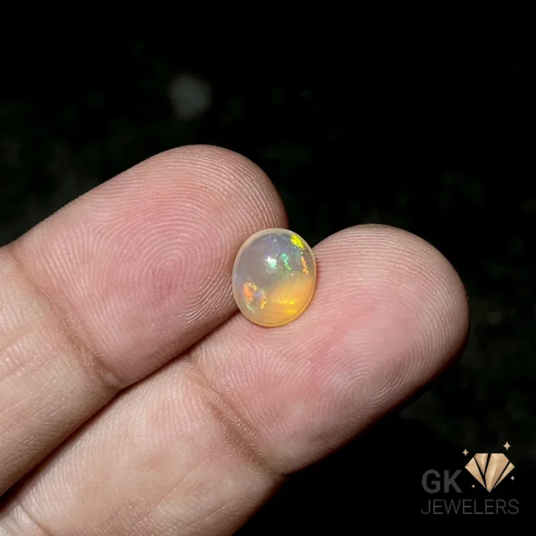 Round opal gemstone with iridescent colors on a person's finger