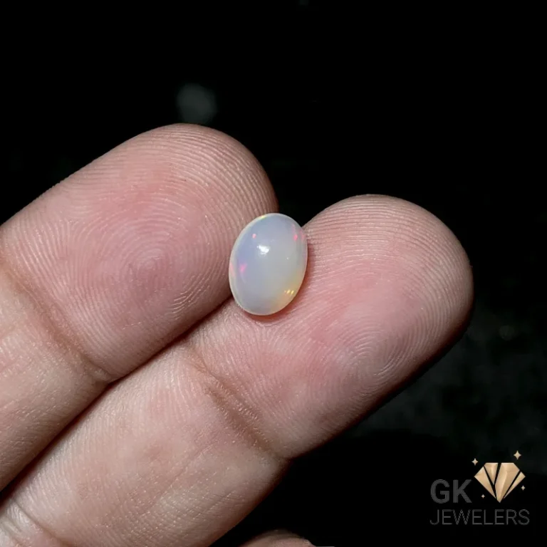 Oval white opal gemstone held between fingers, displaying subtle rainbow hues