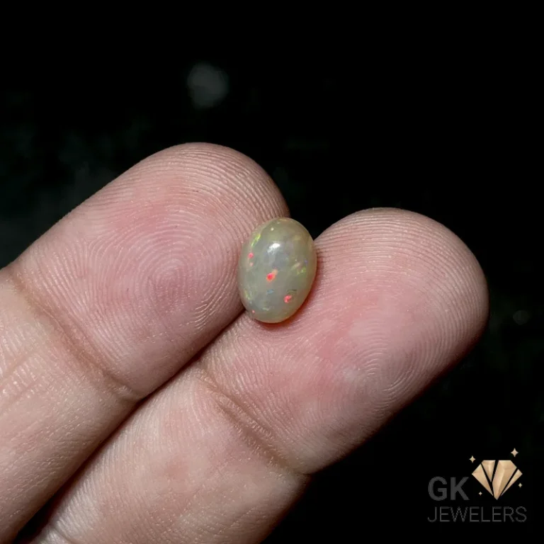 Opal gemstone with vibrant red and green flecks on fingertips