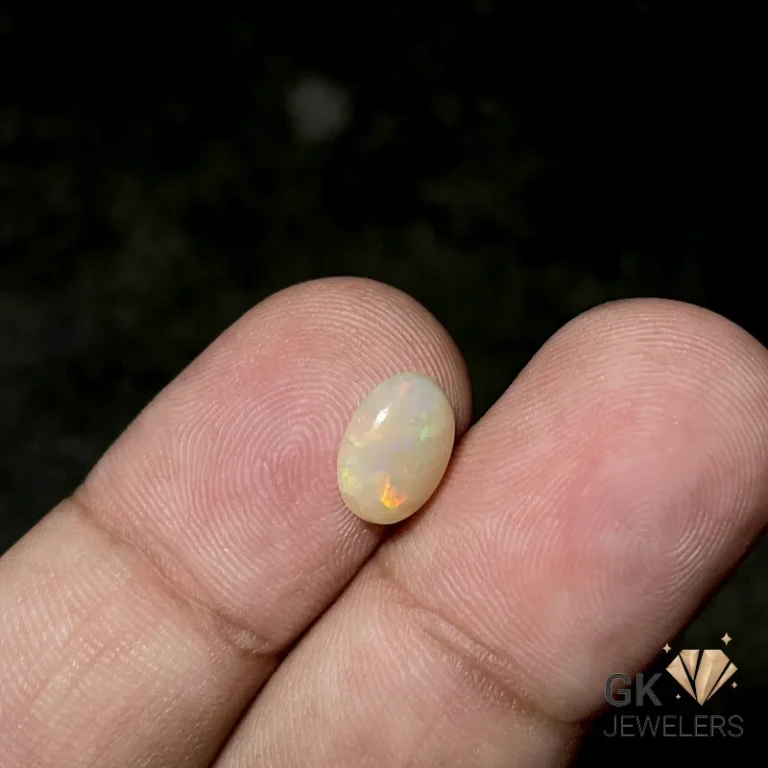 Oval white opal gemstone with iridescent fire held between fingertips