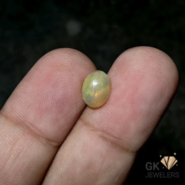 Oval opal gemstone held between fingertips on a dark surface