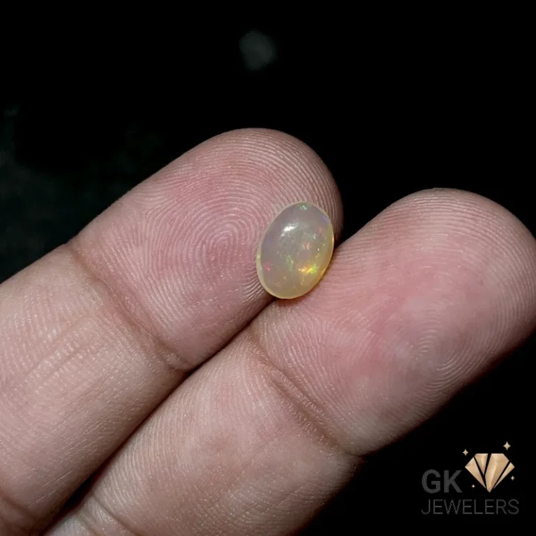 Oval opal gemstone resting on fingertips against a dark background