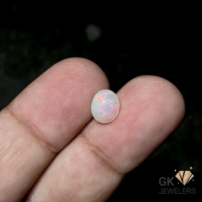 Oval opal gemstone resting on fingertips against dark background