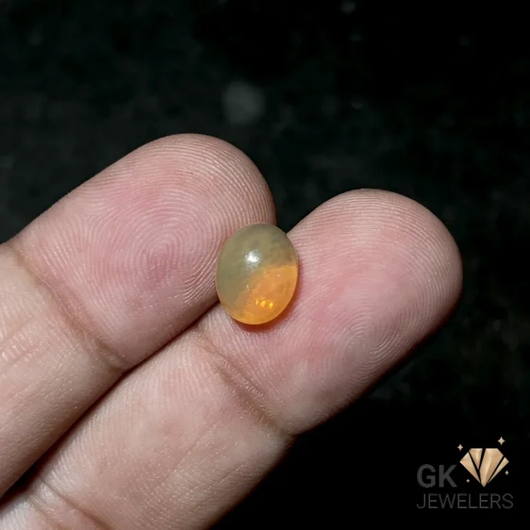 Oval orange opal gemstone held between fingers with subtle sheen
