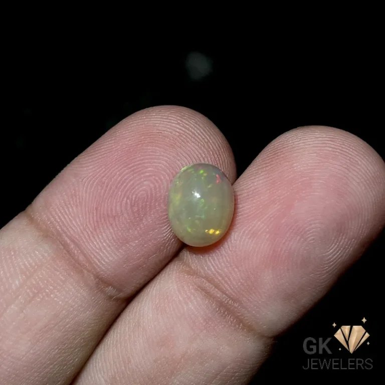 Oval white opal gemstone with multicolored specks held between fingertips
