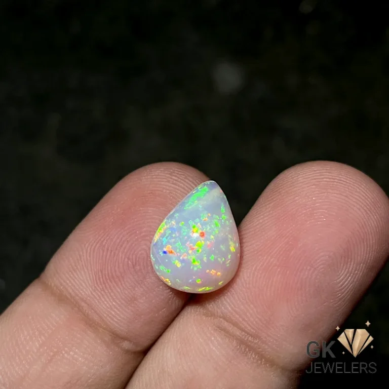 Teardrop-shaped white opal gemstone with vibrant green and orange fire held between fingers