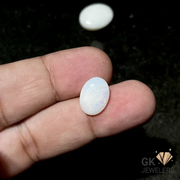 Opal gemstone held between fingers on a dark background