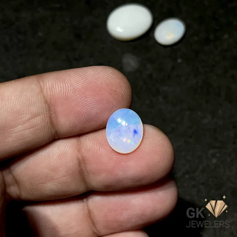 Oval opal gemstone held between fingertips on a dark background