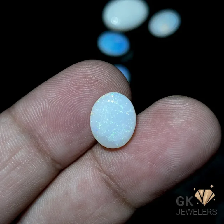White opal gemstone held between fingers on a black background with other opals
