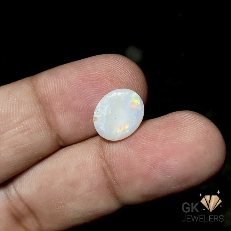 White opal gemstone held between person's fingers, showcasing iridescent colors