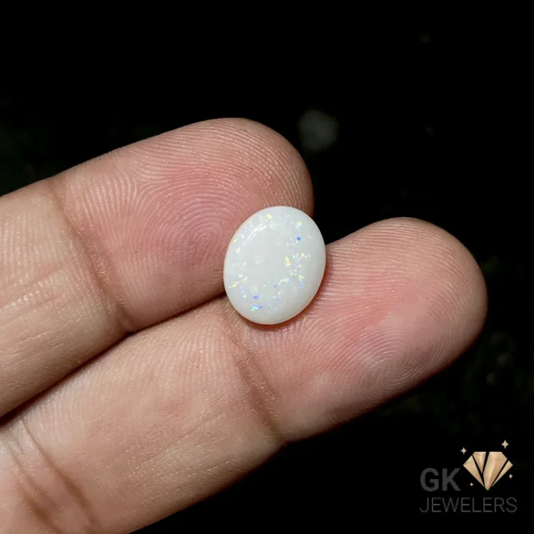 Oval white opal gemstone with iridescent flecks held between fingers