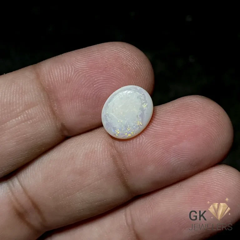 Oval white opal gemstone with gold flecks held between fingers