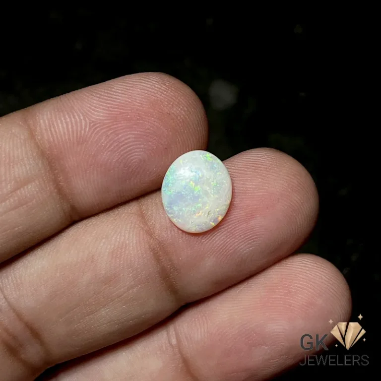 Oval opal gemstone held between fingers, displaying iridescent colors