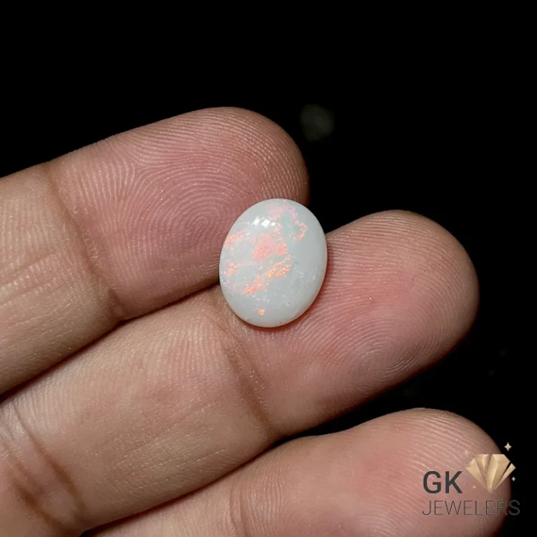 White opal gemstone with orange flecks held between fingers