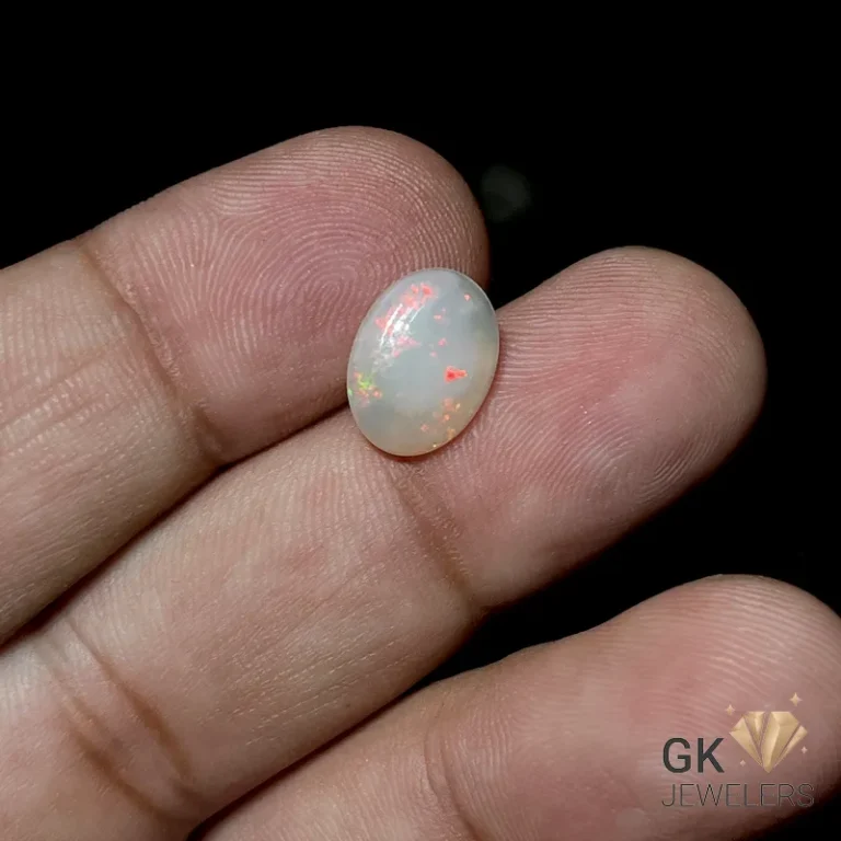 Oval white opal gemstone with vibrant red and green fire held between fingers