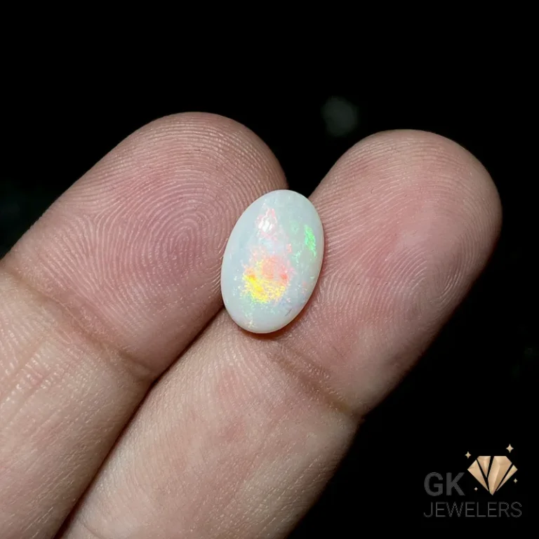 White opal gemstone with iridescent colors held between fingers