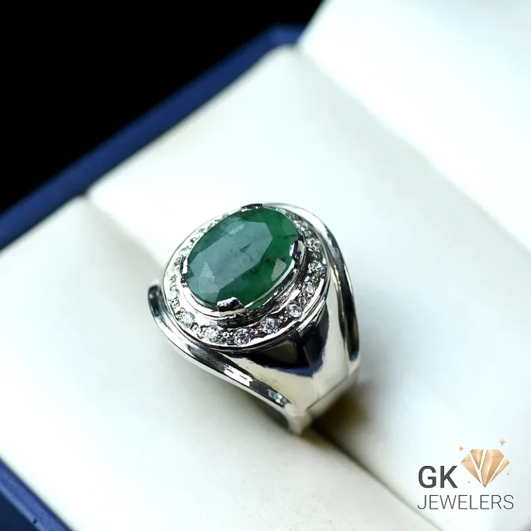 Silver ring with oval emerald and diamond halo on white jewelry box
