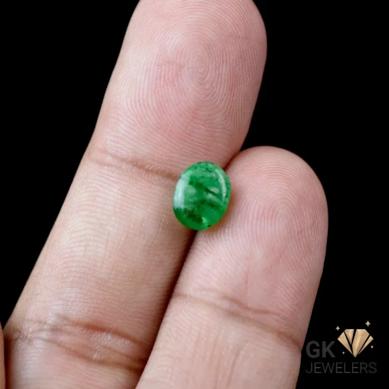 Emerald gemstone resting on fingertips against dark background