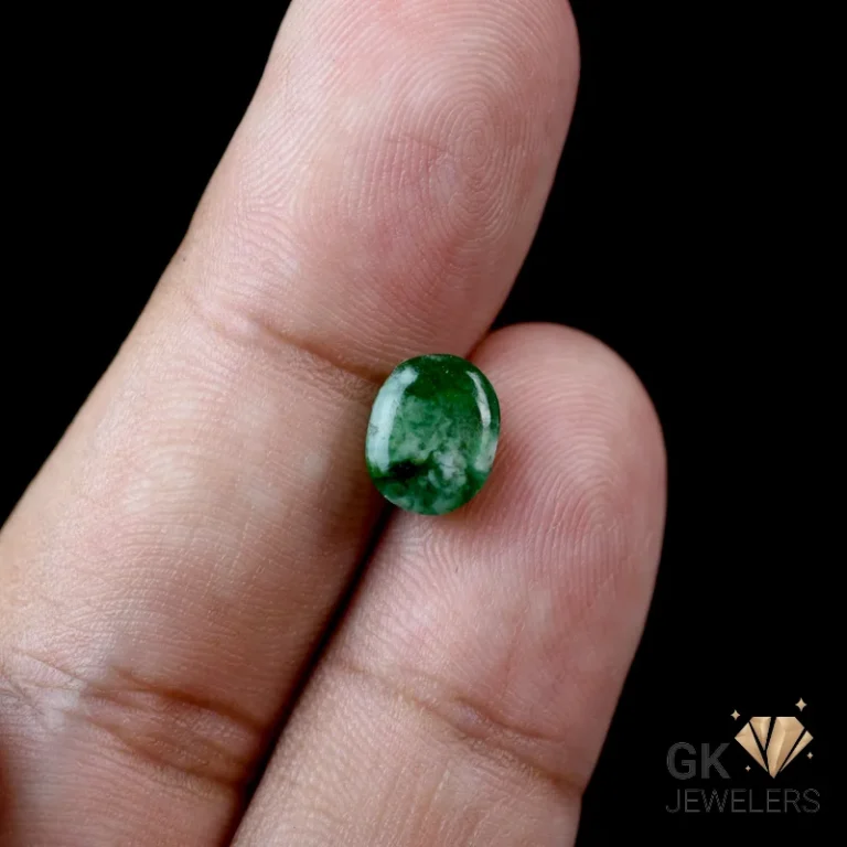 Dark green oval-cut emerald gemstone between thumb and index finger
