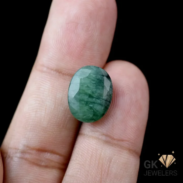 Oval-cut emerald gemstone held between fingers