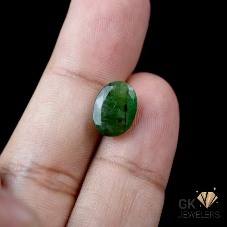 Oval-cut emerald gemstone held between fingers