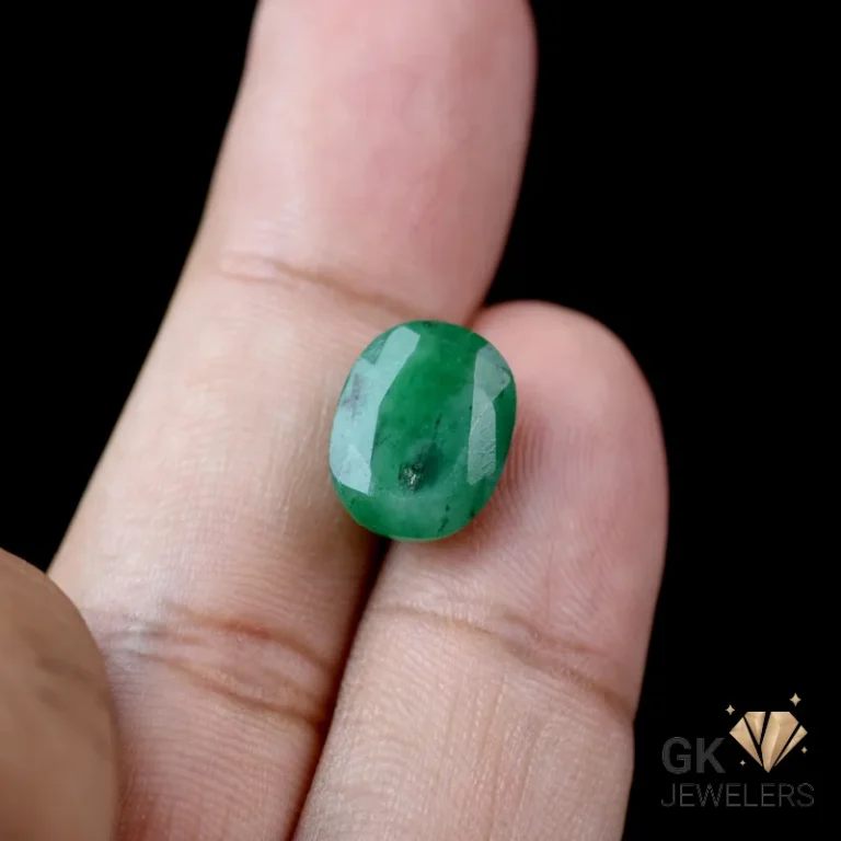 Emerald gemstone cabochon held between fingers on a black background