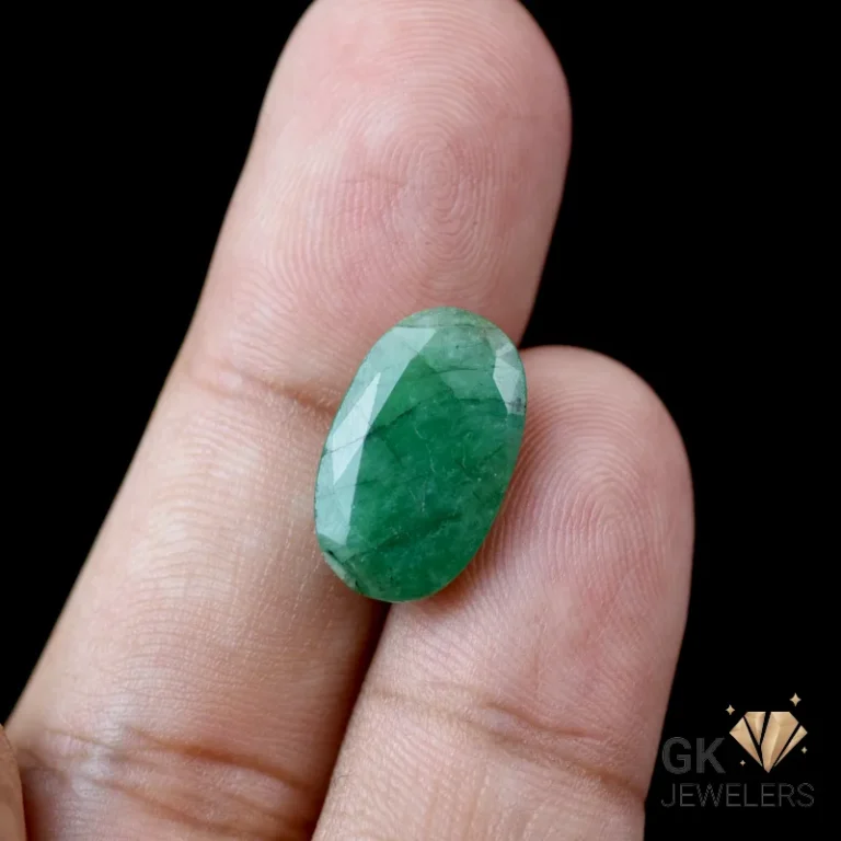 Oval-cut emerald gemstone held between fingers against a black background
